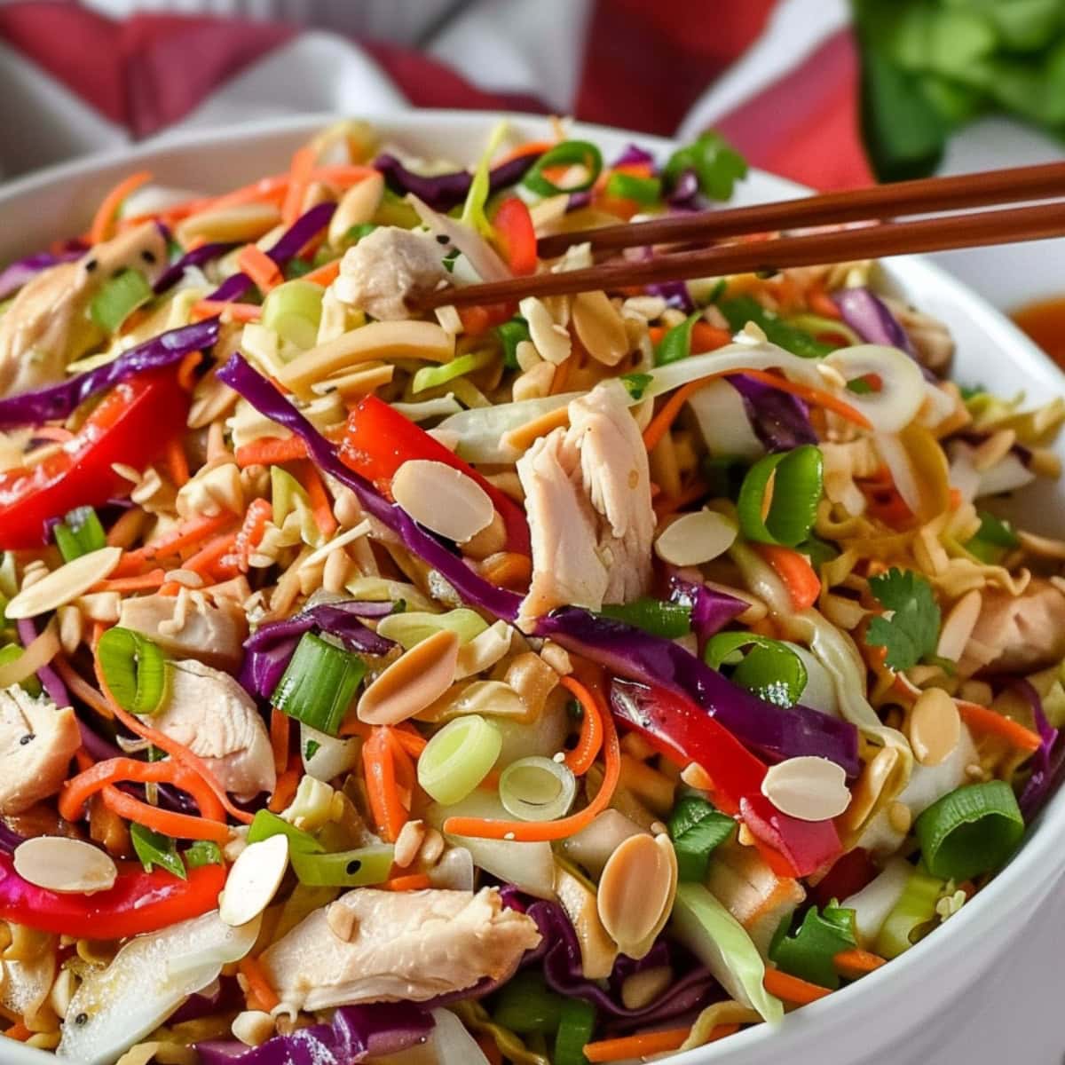 Pair of wooden chopsticks scooping in a bowl of Chinese chicken salad.
