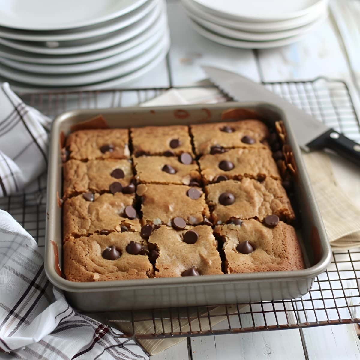 Chocolate Chip Blondies in the Baking Dish on a Wire Rack with a Knife and Plates for Serving in the Background