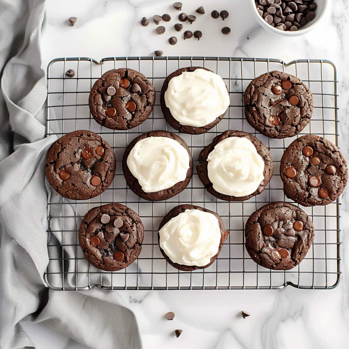 Chocolate cookies on a cooling rack. Half are covered in vanilla cream filling. Top down view