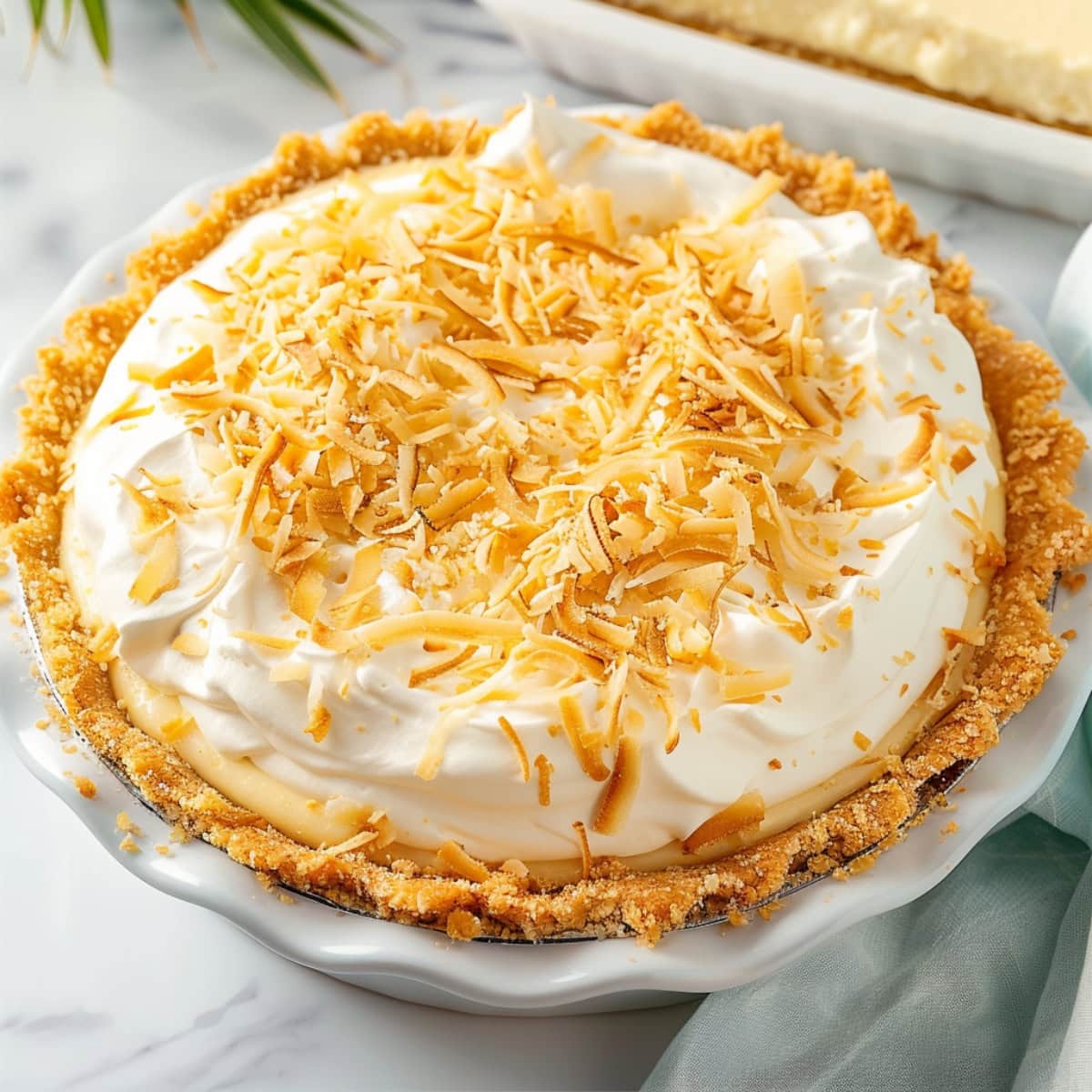 Whole coconut cream pie in a white pie dish garnished with toasted shredded coconut.