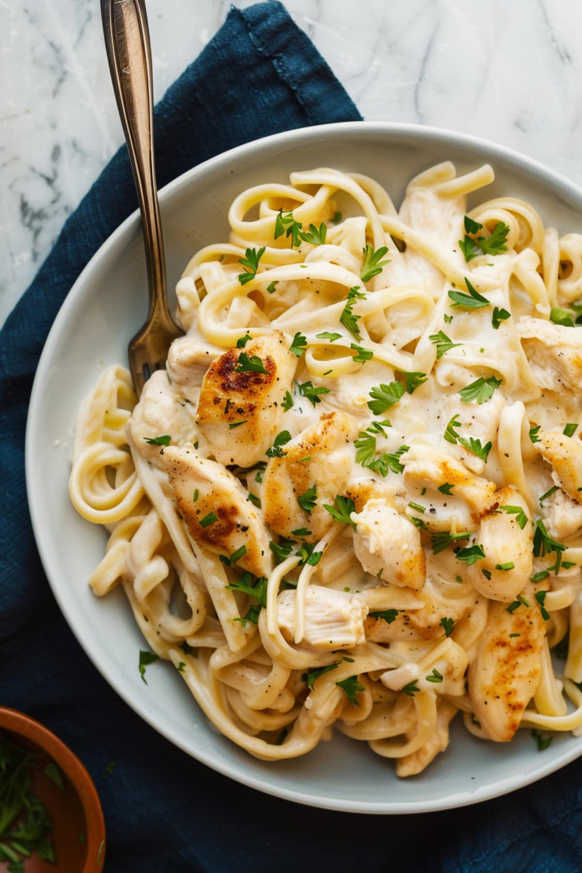 Chicken alfredo fettucine pasta with chicken pieces and garnished with parsley.