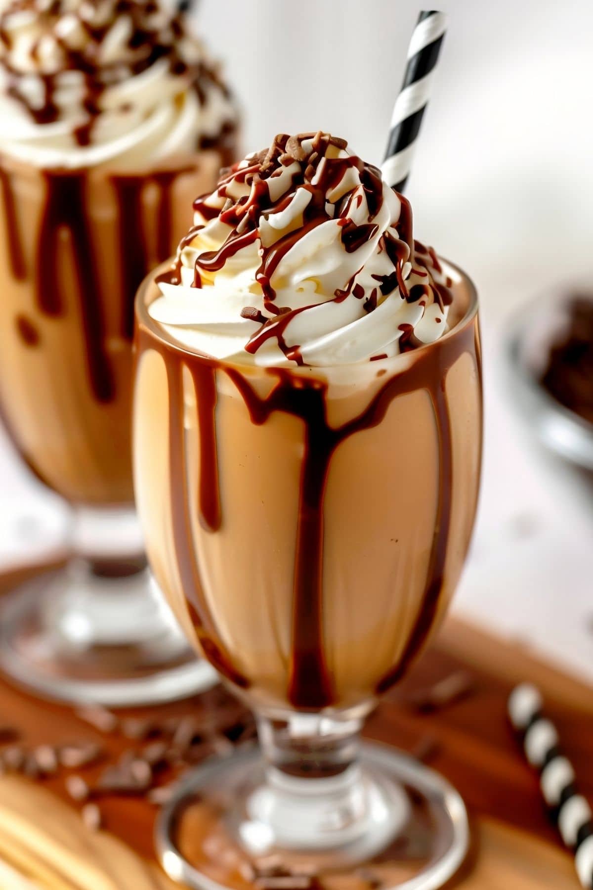 Two Frozen Mudslides in Tall Glasses with a Chocolate Drizzle, Whipped Cream, and More Chocolate on Top