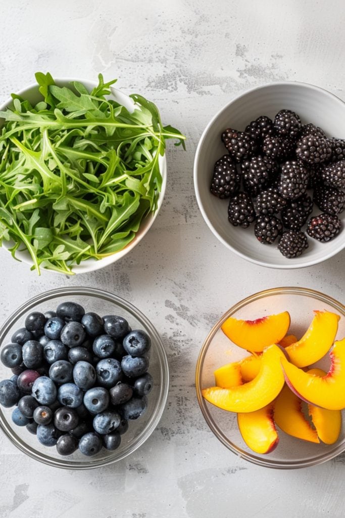 Arugula leaves, berries and peach wedges arranged on a white marble table.