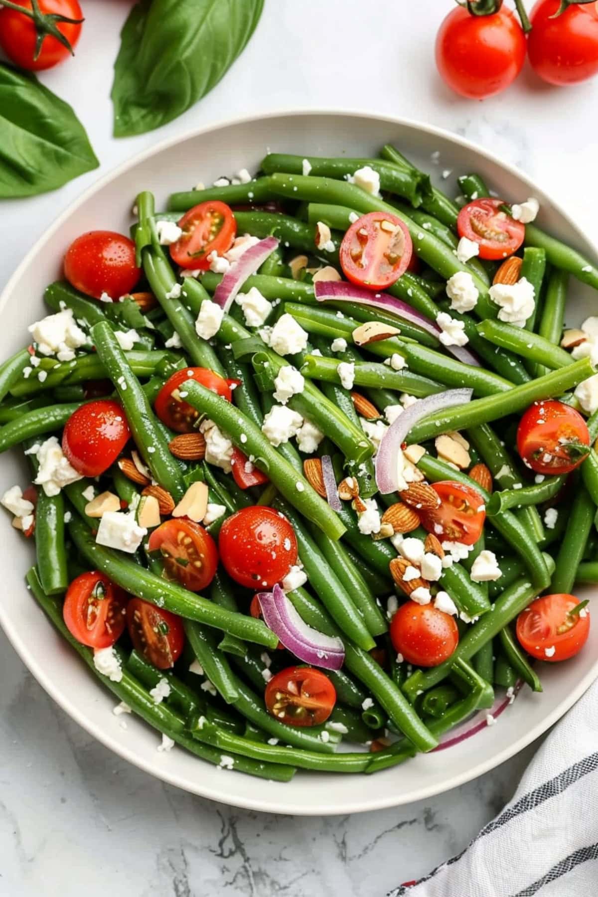 Green bean salad with cherry tomatoes, nuts, onions and feta cheese in a white bowl.