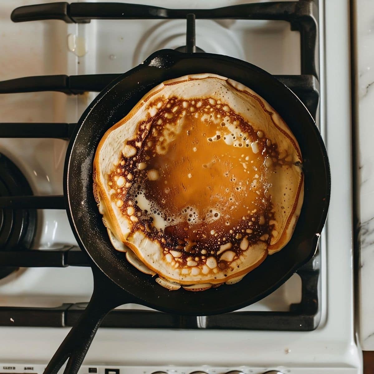 Top View of IHOP Pancake Recipe Pancake Cooking on a Stove in a Cast Iron Pan