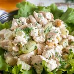 Close Up of Ina Garten's Chicken Salad with Chicken, Dill, Celery, and Mayo on a Bed of Lettuce with a Glass of Tea in the Background