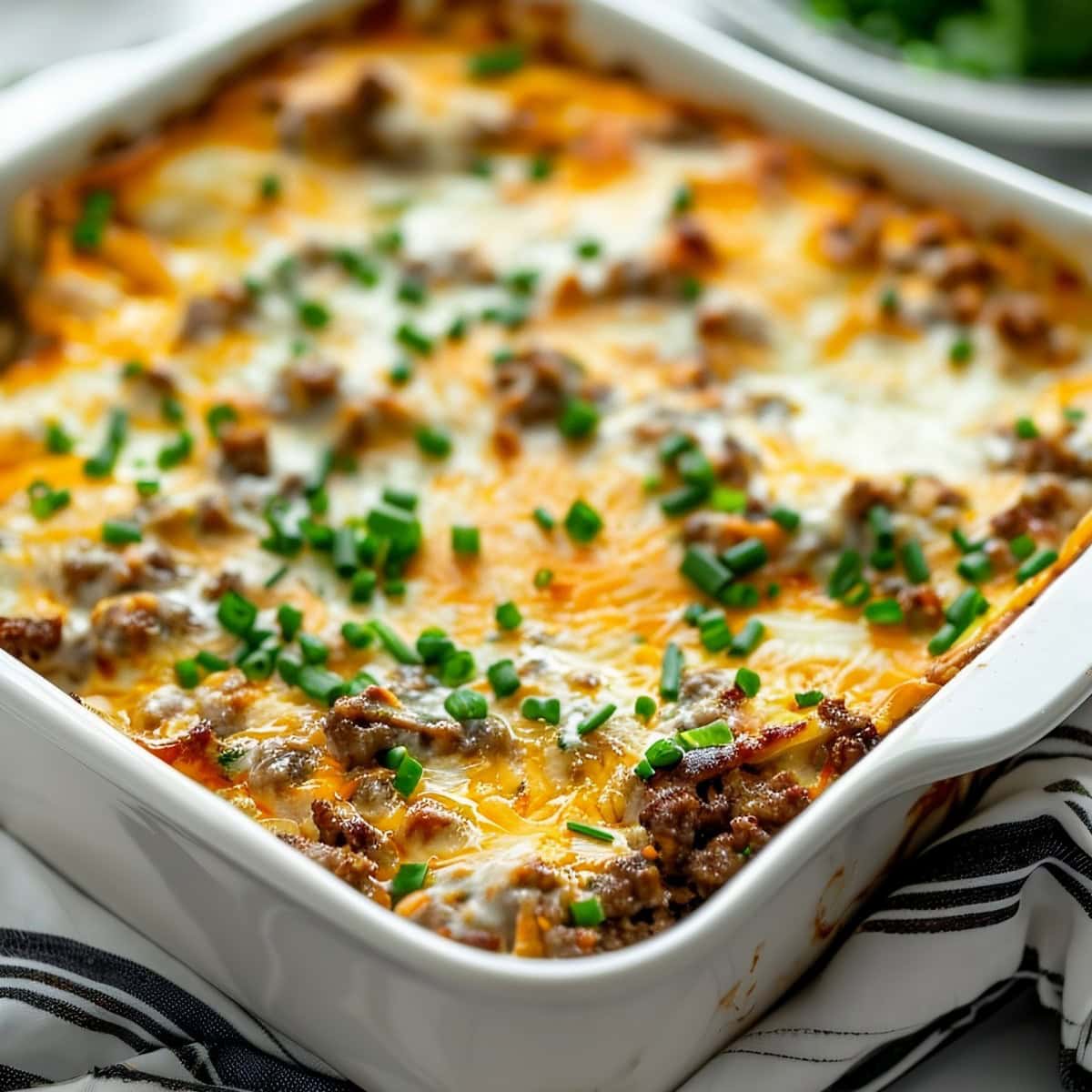 Close Up of Cheesy Italian Sausage Breakfast Casserole in a Casserole Dish, Garnished with Green Onions