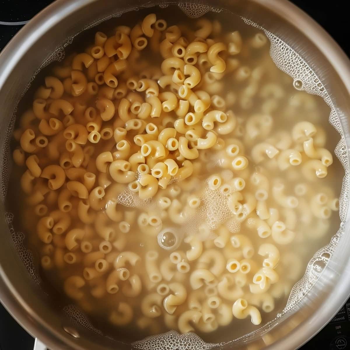 Top View Macaroni Noodles Cooking in Boiling Water in a Saucepan Over the Stove