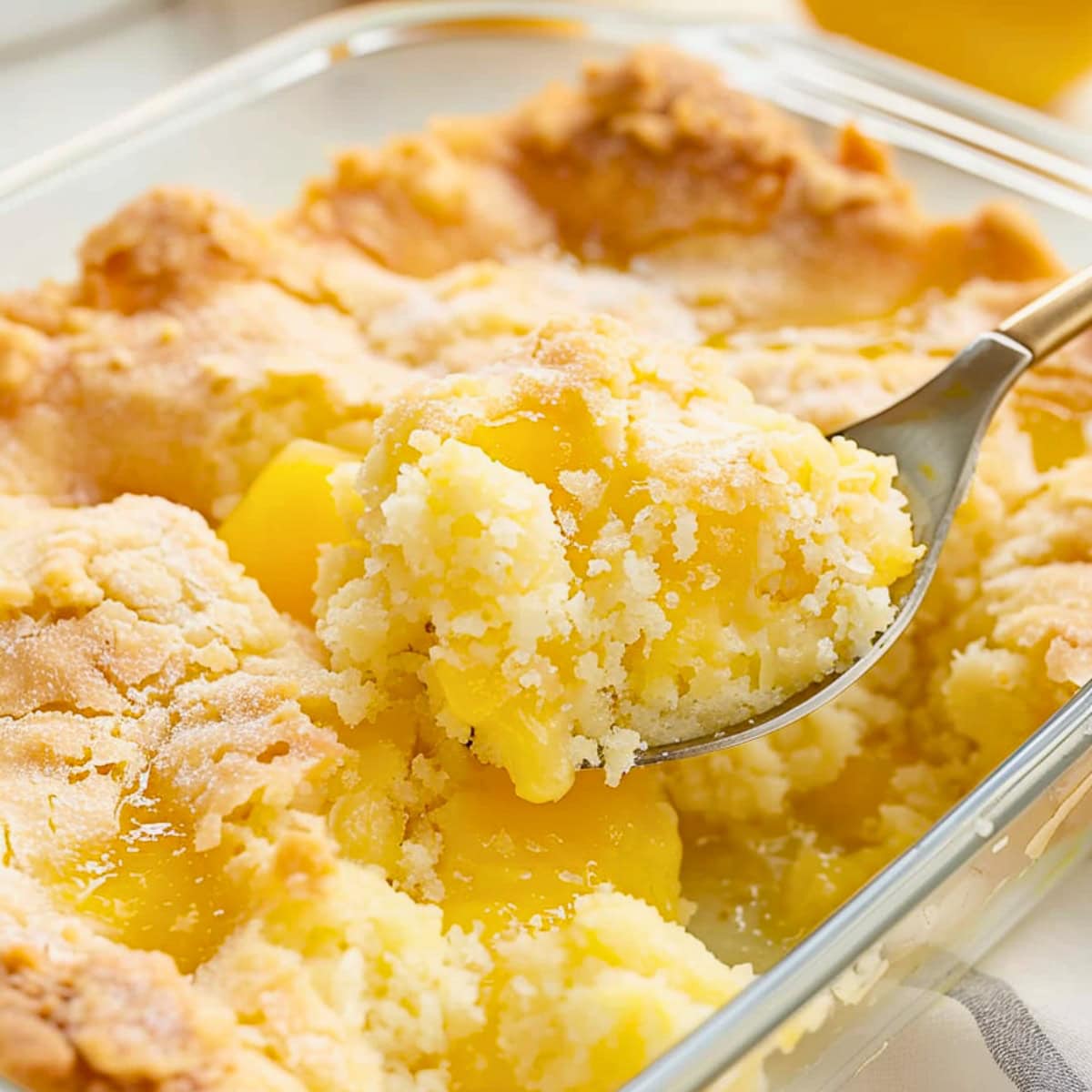 Spoon scooping a serving of lemon cream cheese dump cake from a baking dish.