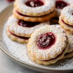 Close Up of Linzer Cookies Dusted with Powdered sugar on a Plate with Fresh Raspberries Around the Plate