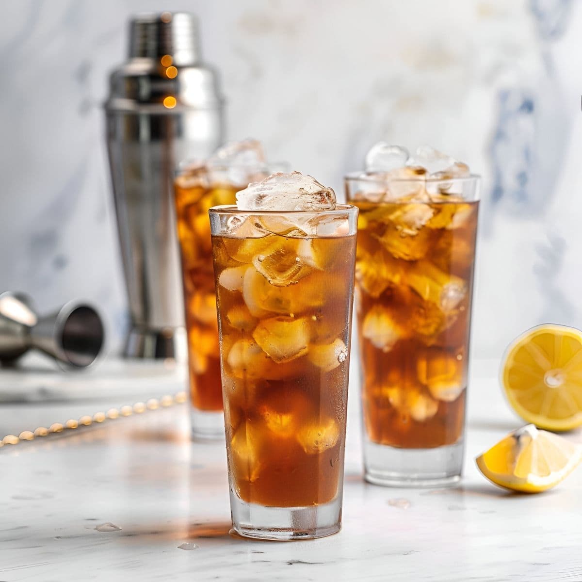 Three Long Island Iced Teas in Tall Glasses with Ice with Cocktail Making Equipment and Lemons in the Background
