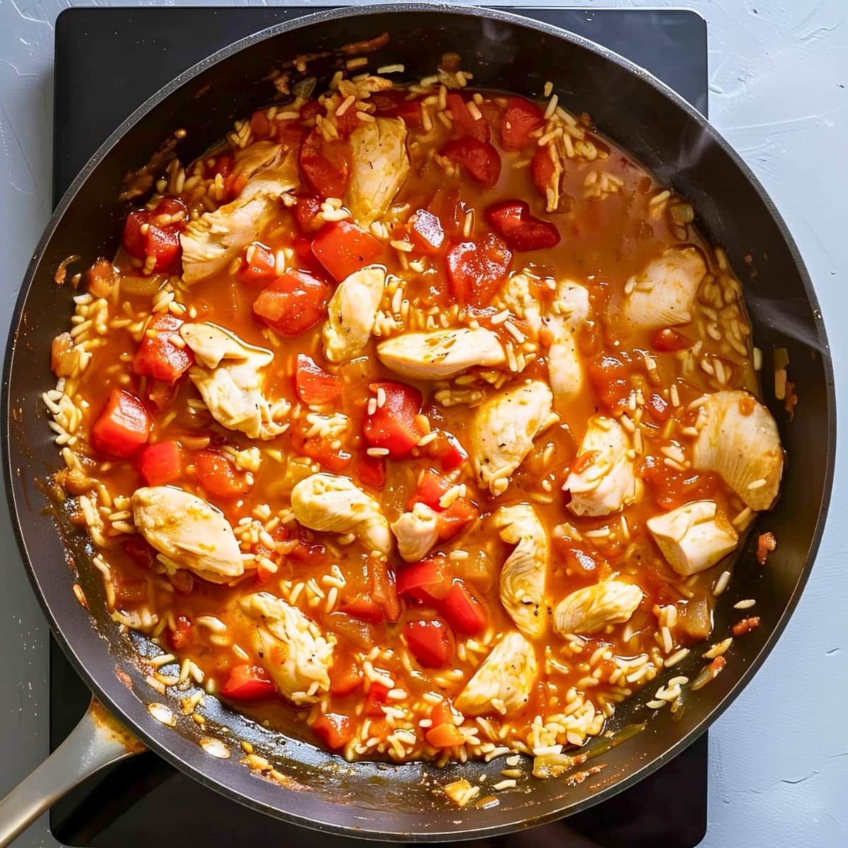 Top View of Chicken, Rice, and Tomatoes in a Skillet over a Hot Plate