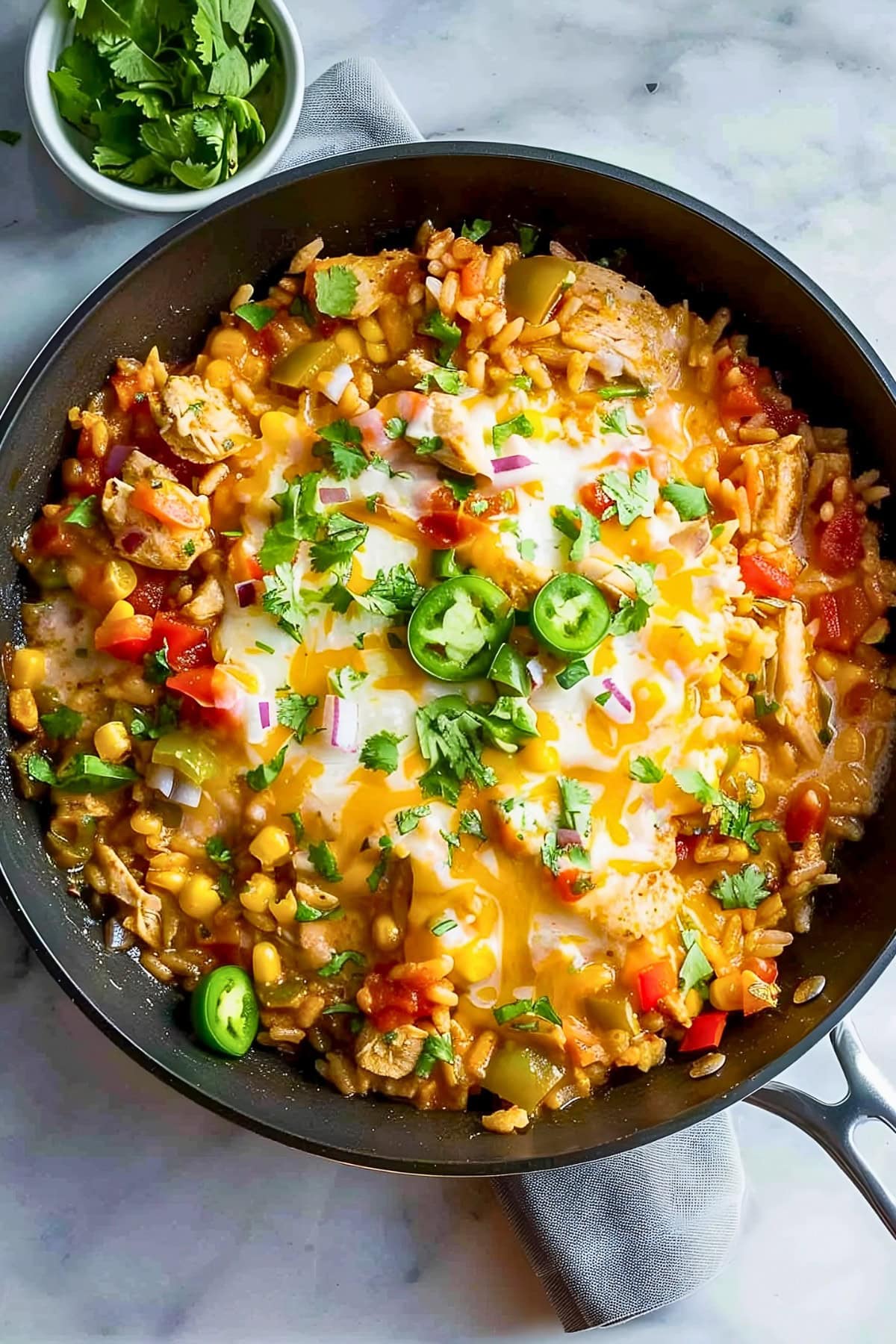 Top View of Mexican Chicken and Rice- Rice, Chicken Tomatoes, Corn, Peppers, and Cheese- In a Skillet, Topped with Fresh Jalapenos and Cilantro