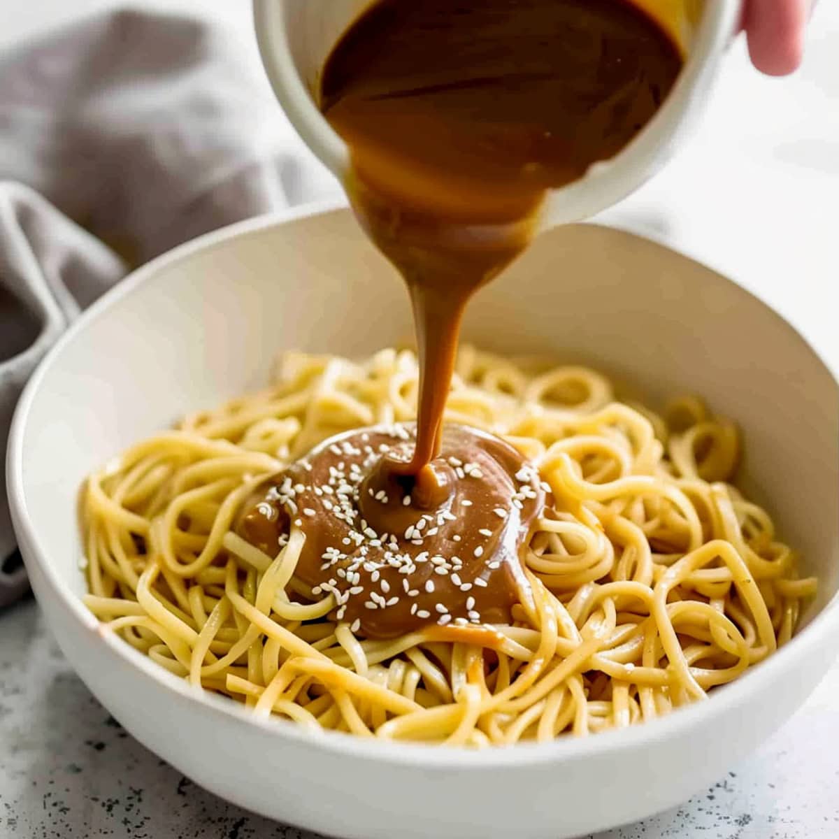 Pouring sesame paste into a bowl of cooked noodles.