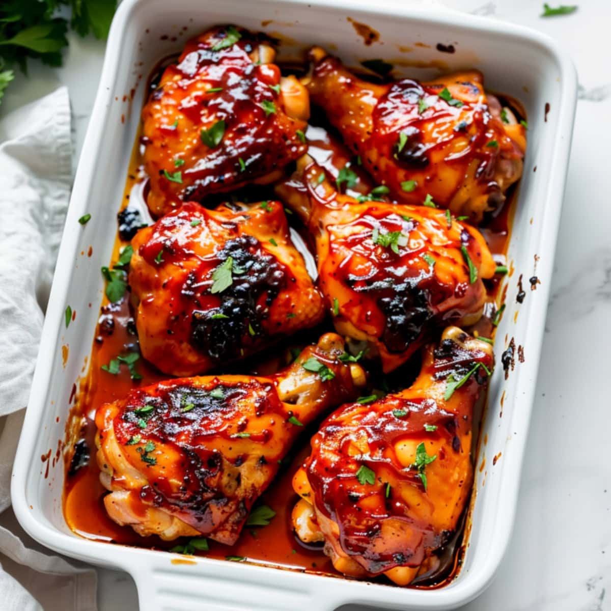 Chicken Drumsticks and thighs covered in bbq marinade in a baking dish.