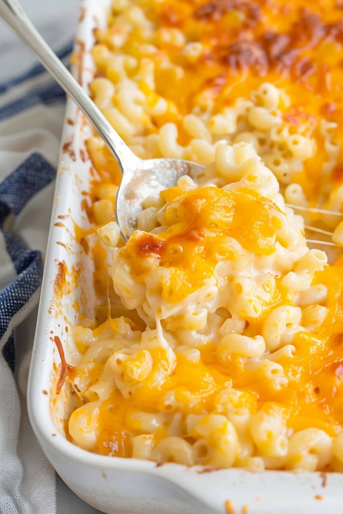 Close Up of Sweetie Pie's Mac and Cheese in a Casserole Dish with a Spoon and a Blue Kitchen Towel