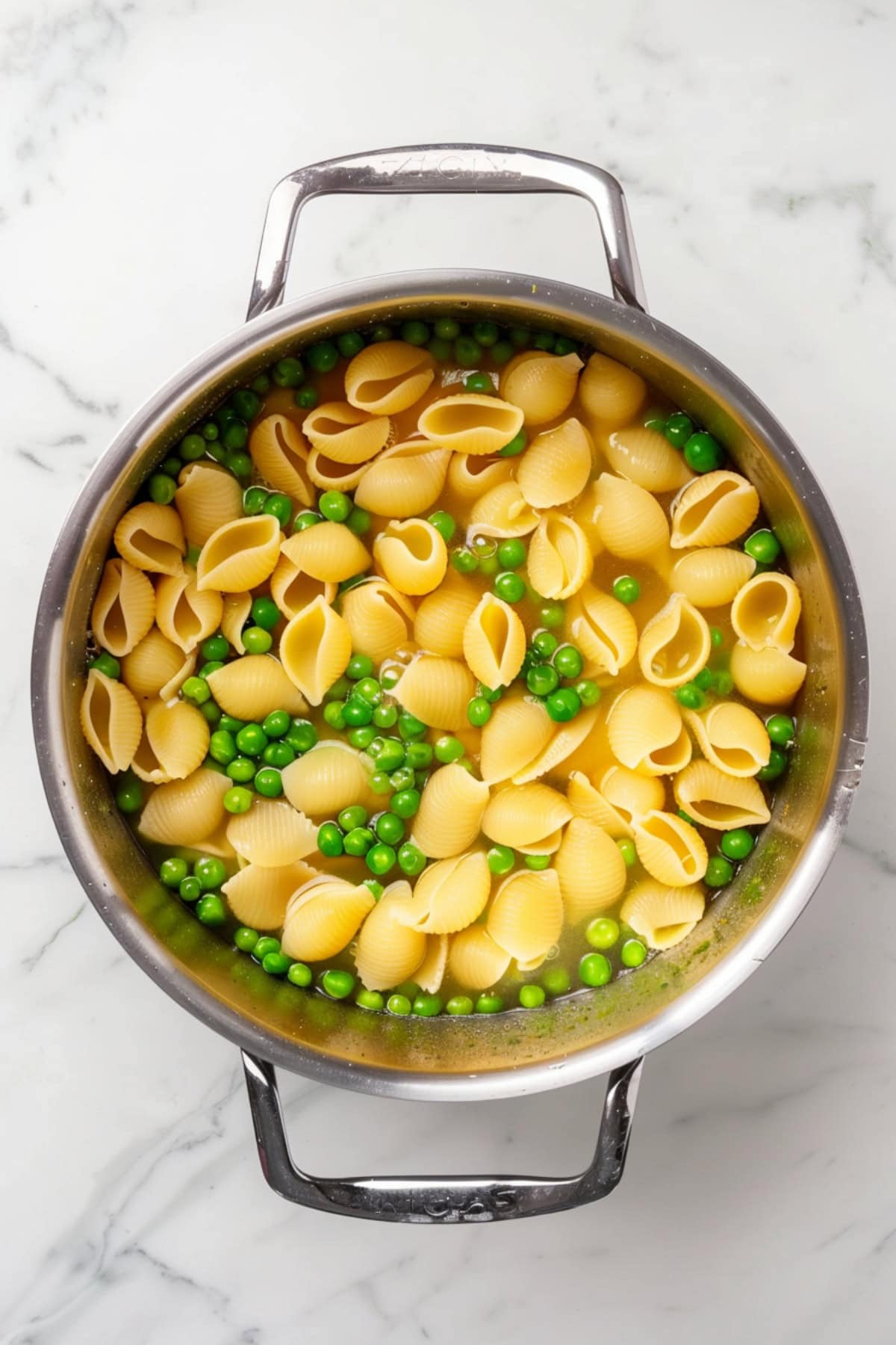 A large pot of boiling water filled with pasta shells and green peas.