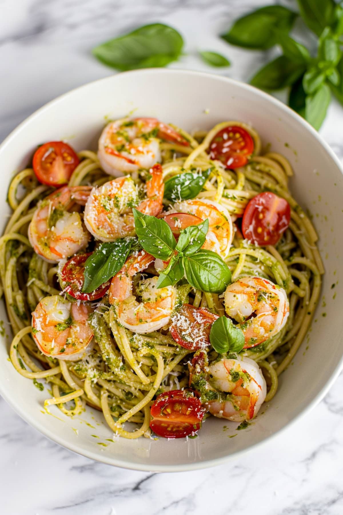 Homemade pasta with shrimp, tomatoes and pesto, garnished with shredded parmesan cheese and basil.