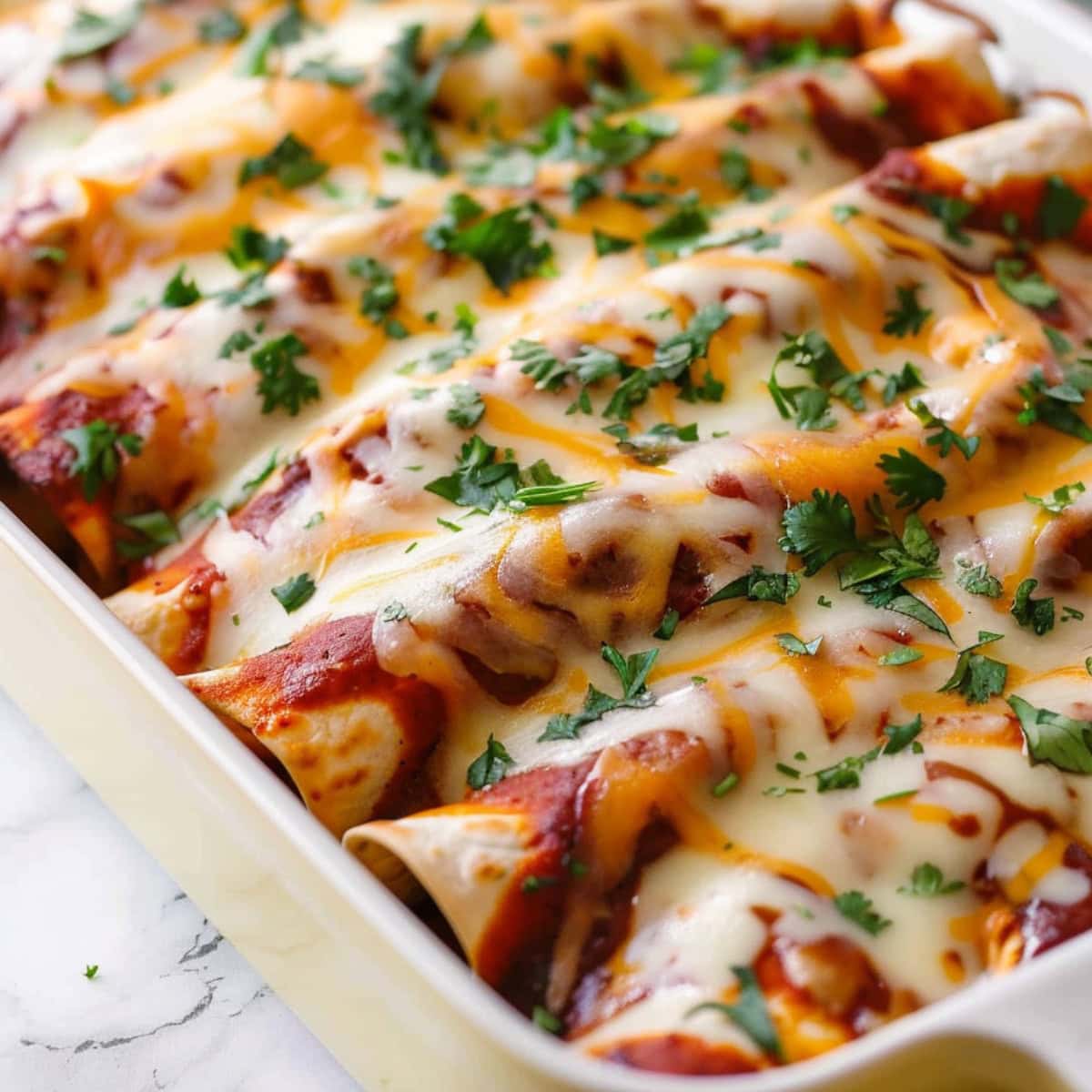 Cheesy pulled pork enchiladas with sauce on a yellow rectangular baking dish.