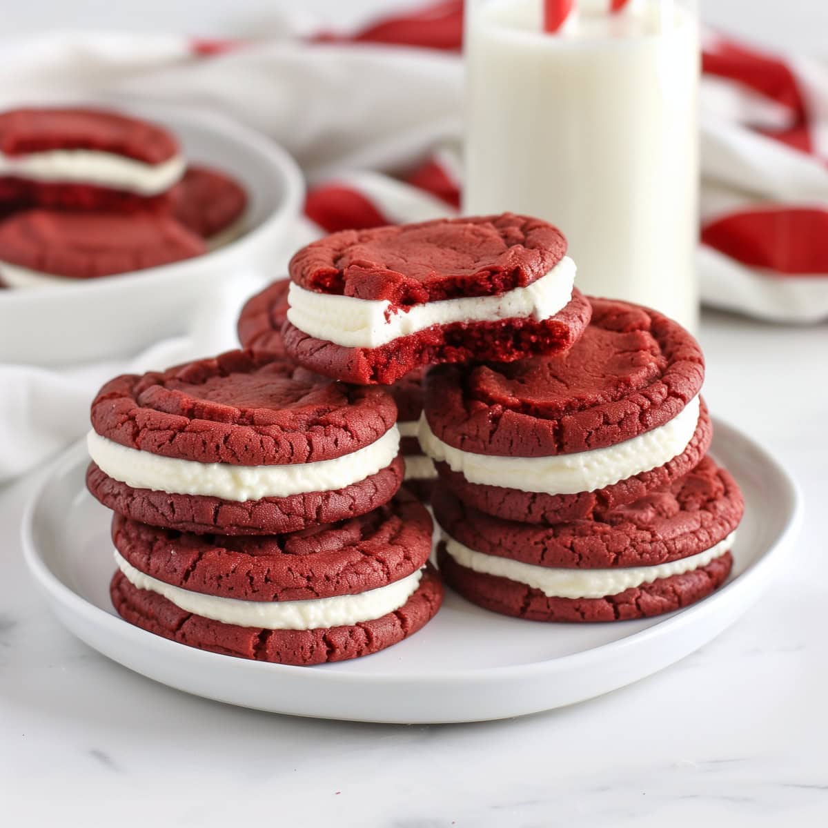 Decadent red velvet sandwich cookies featuring a smooth cream cheese filling with milk on the side.