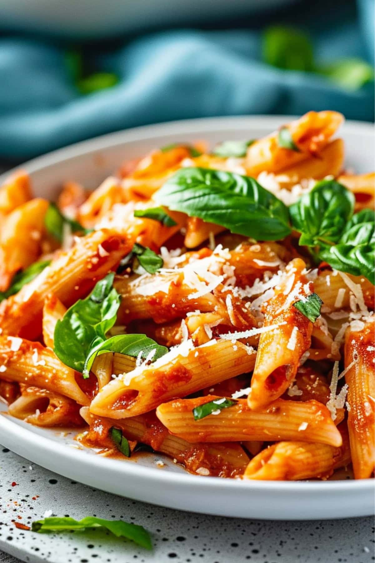 Serving of roasted red pepper pasta in a white plate garnished with fresh basil leaves. 