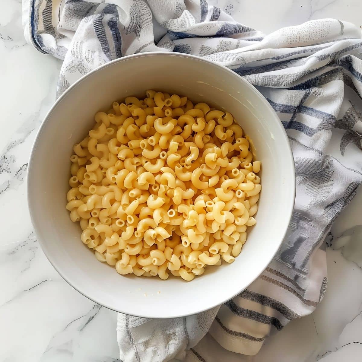 Top View of Plain, Cooked Macaroni Noodles in a White Bowl on a White Marble Table