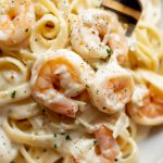 Super Close Up of Shrimp Alfredo- with Fettuccine, Pink Shrimp, White Sauce, and Herbs- on a Plate with a Fork