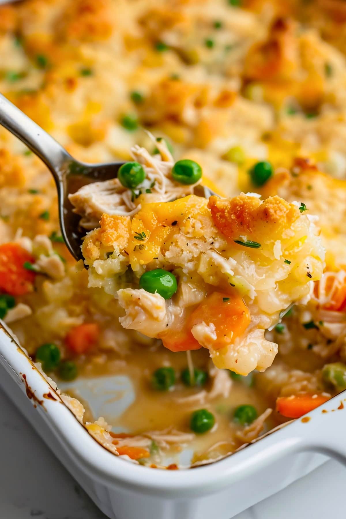 Close Up of a Bite of TikTok Chicken Cobbler on a Spoon Over a Casserole Dish of TikTok Chicken Cobbler