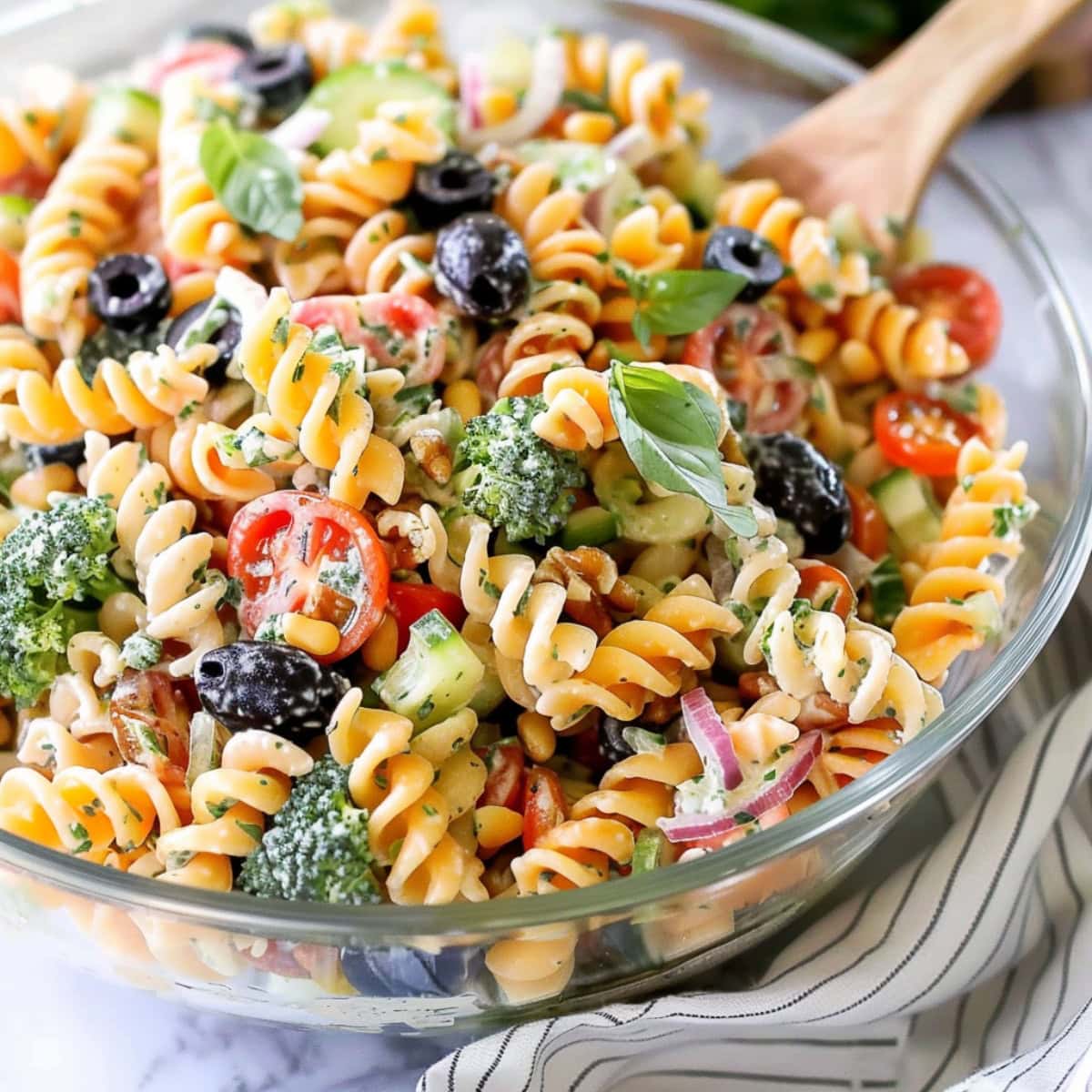 Tri color pasta salad with with fresh herbs, pesto, veggies, cheese and tri color rotini pasta tossed in caesar salad tossed in glass bowl.  
