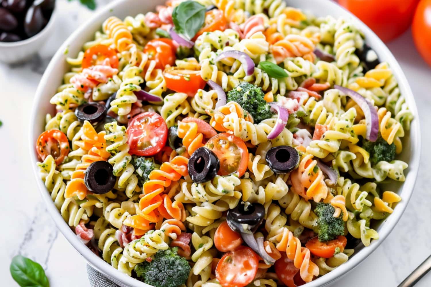 Tri color pasta salad served in a white bowl made with Tri color rotini pasta salad with creamy dressing, rotini pasta with fresh herbs, pesto, veggies, and cheese