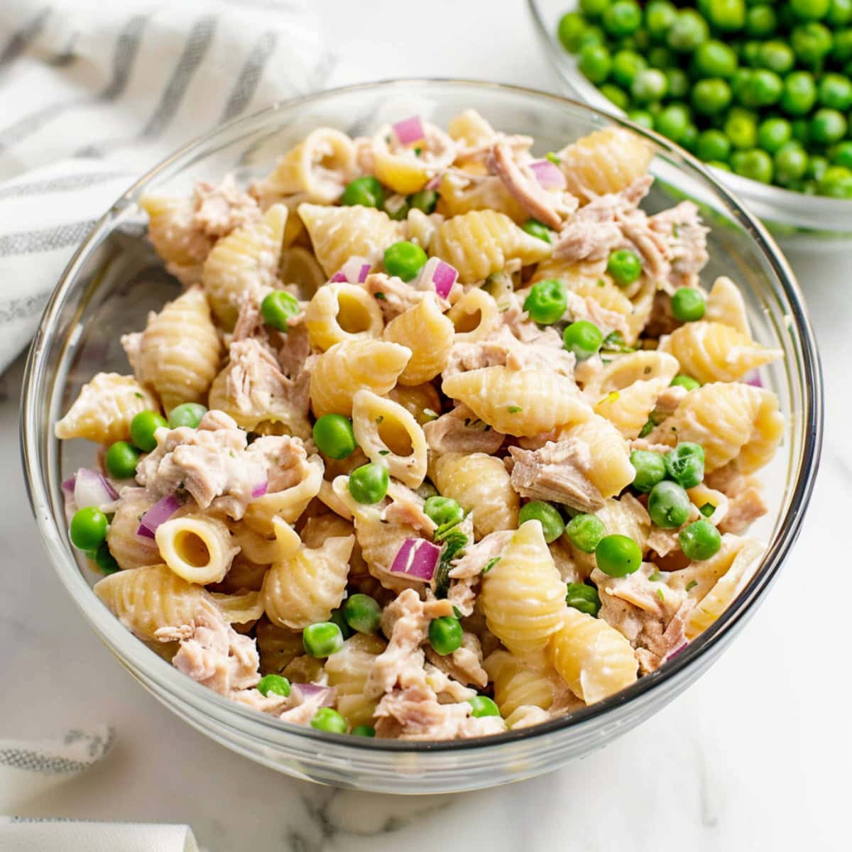 Creamy homemade tuna pasta salad in a glass bowl with green peas on the side.