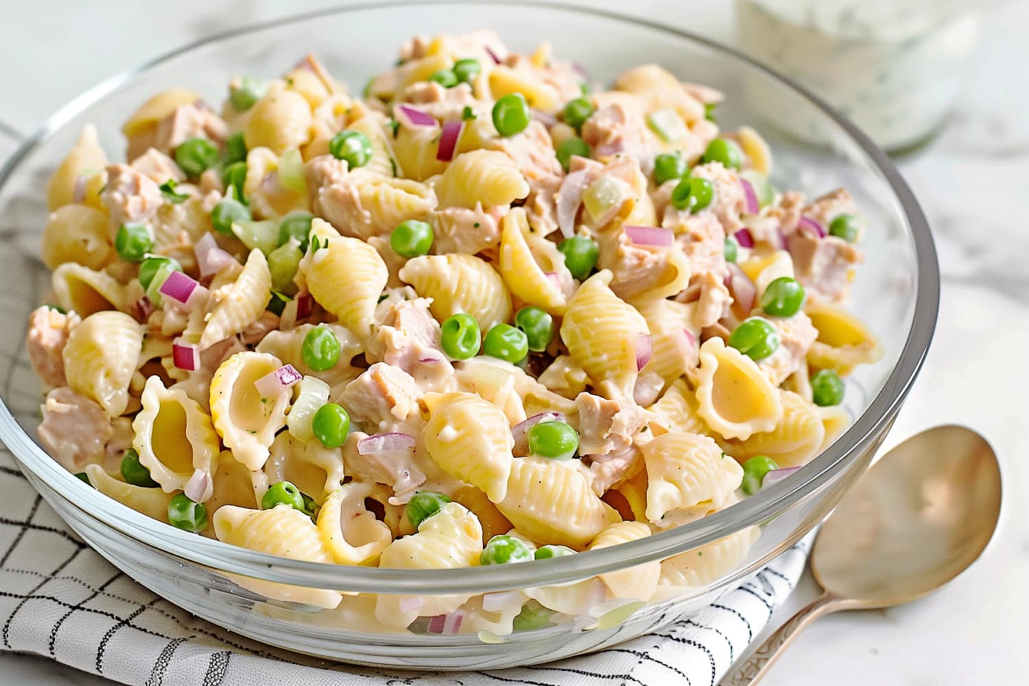A glass bowl of creamy homemade tuna pasta salad on a white marble table.