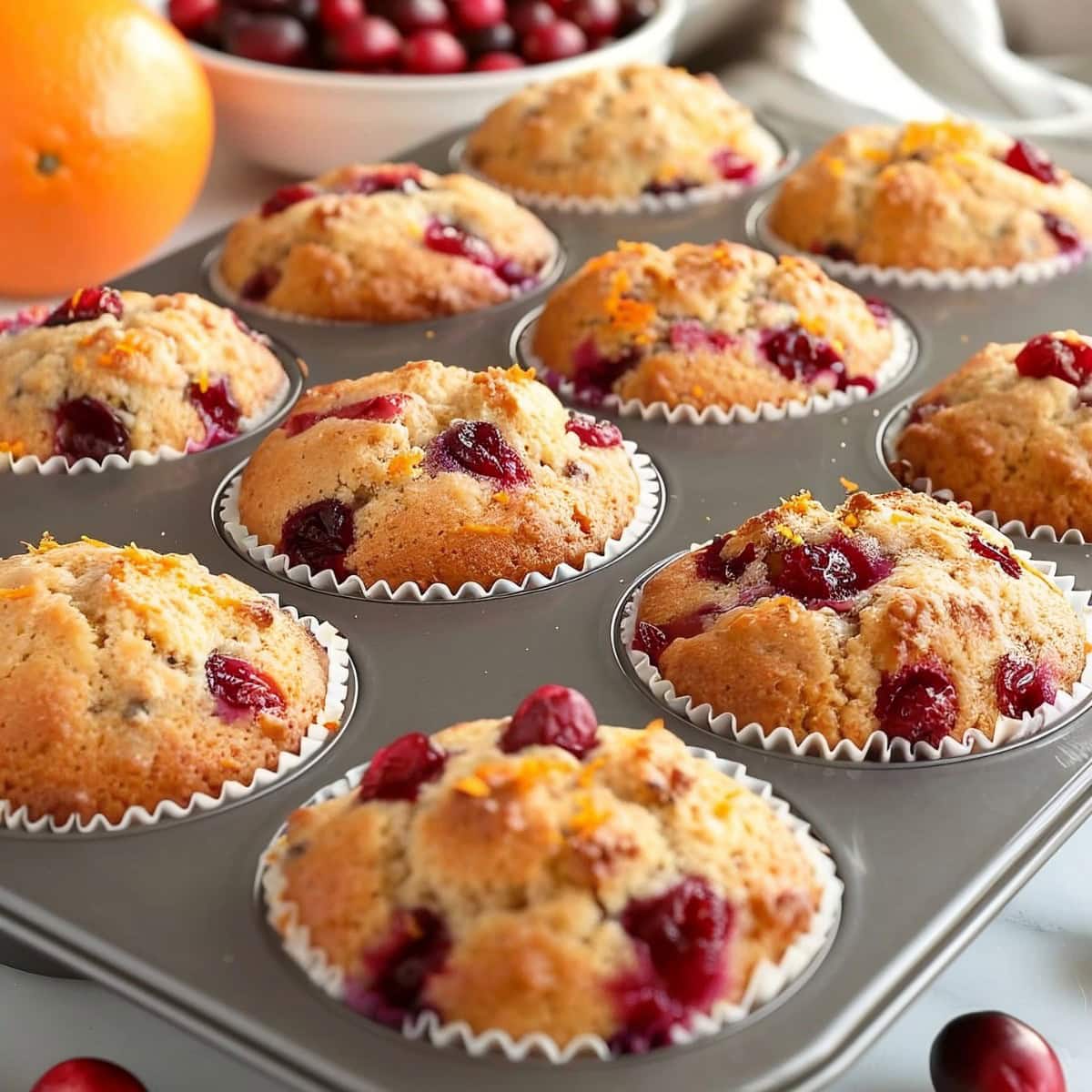 Close Up Cranberry Orange Muffins in a Muffin Tray with Oranges and Cranberries in the Background