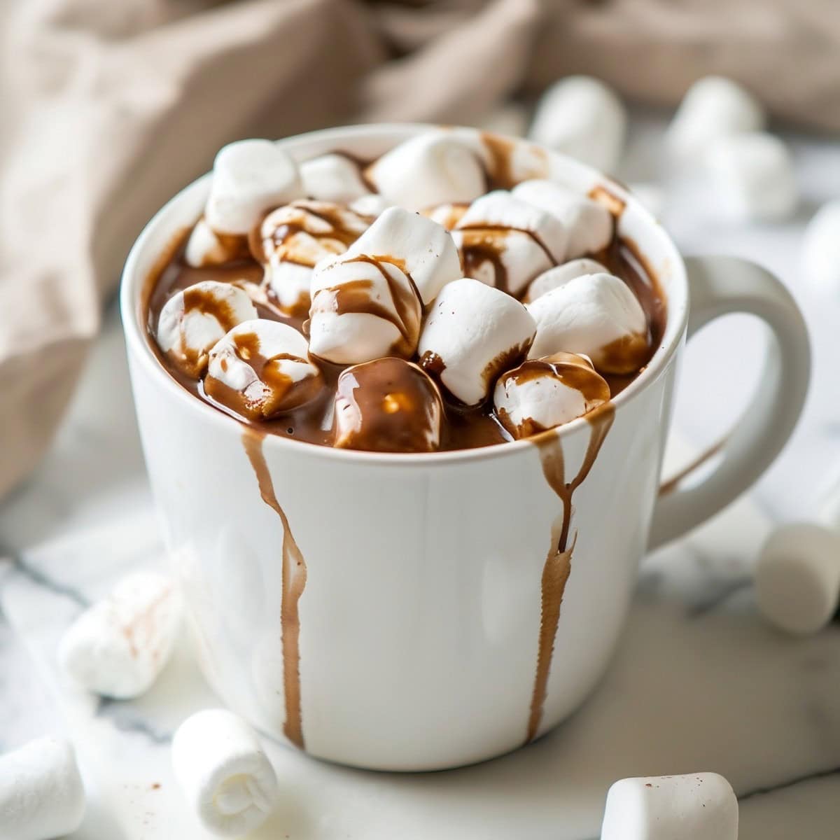 Mug of Crockpot Hot Chocolate with Marshmallows on a White Marble Table with More Marshmallows Around the Mug