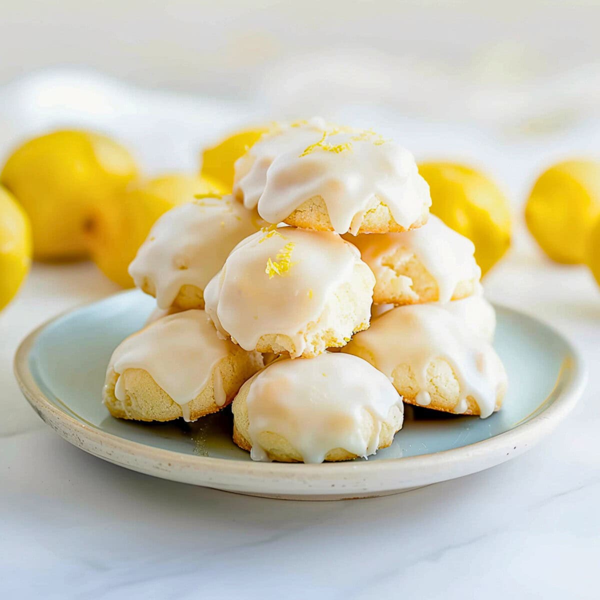 Pile of Lemon Drop Cookies with Lemon Icing on a Plate with Fresh Lemons in the Background