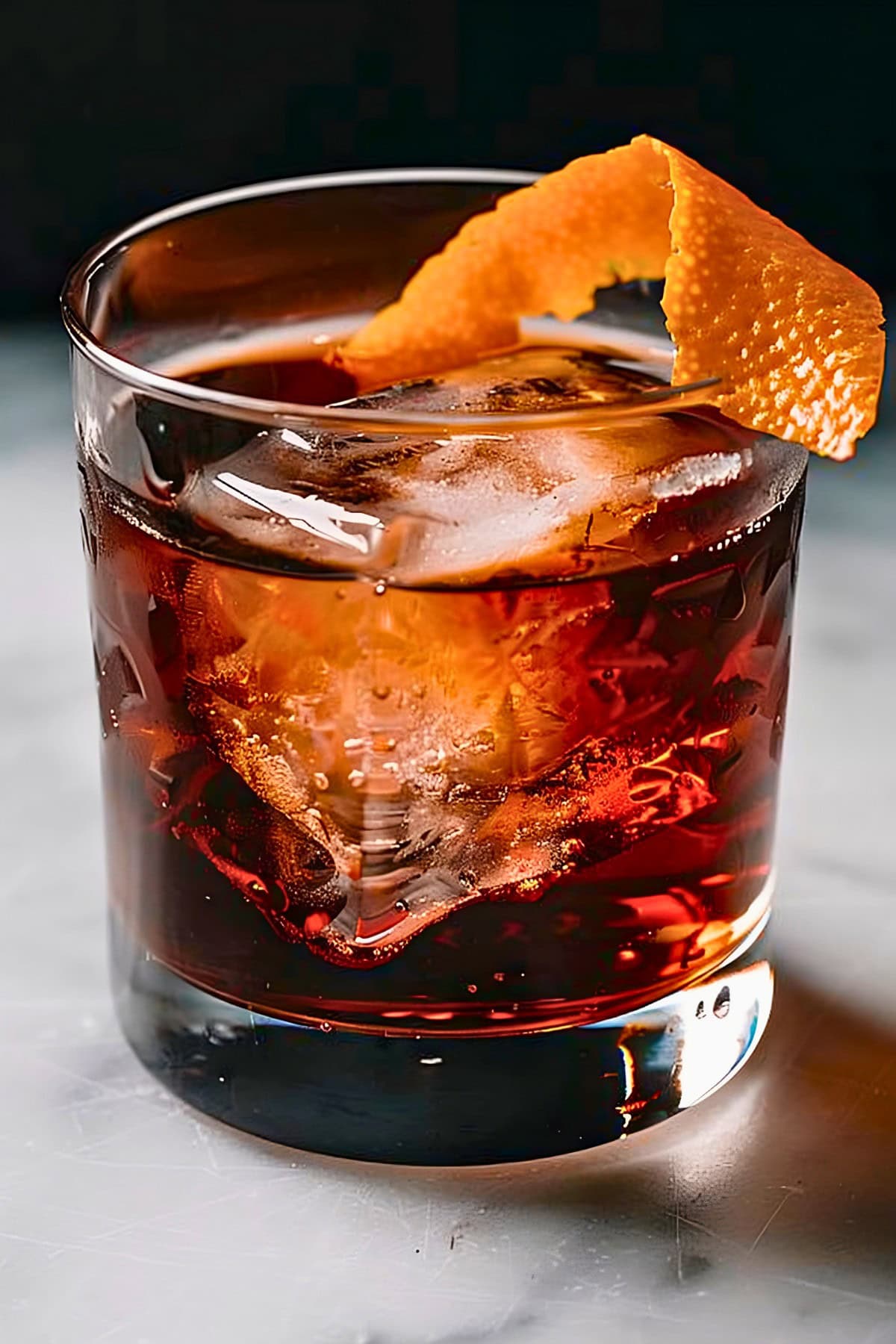 Close Up of a Glass of Reddish-Orange Mezcal Negroni in a Rocks Glass with Ice and an Orange Peel for Garnish