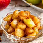 Close Up of Cinnamon-Spiced Microwave Baked Apples in a Glass Dish on a Table with Fresh Apples and Cinnamon Sticks in the Background