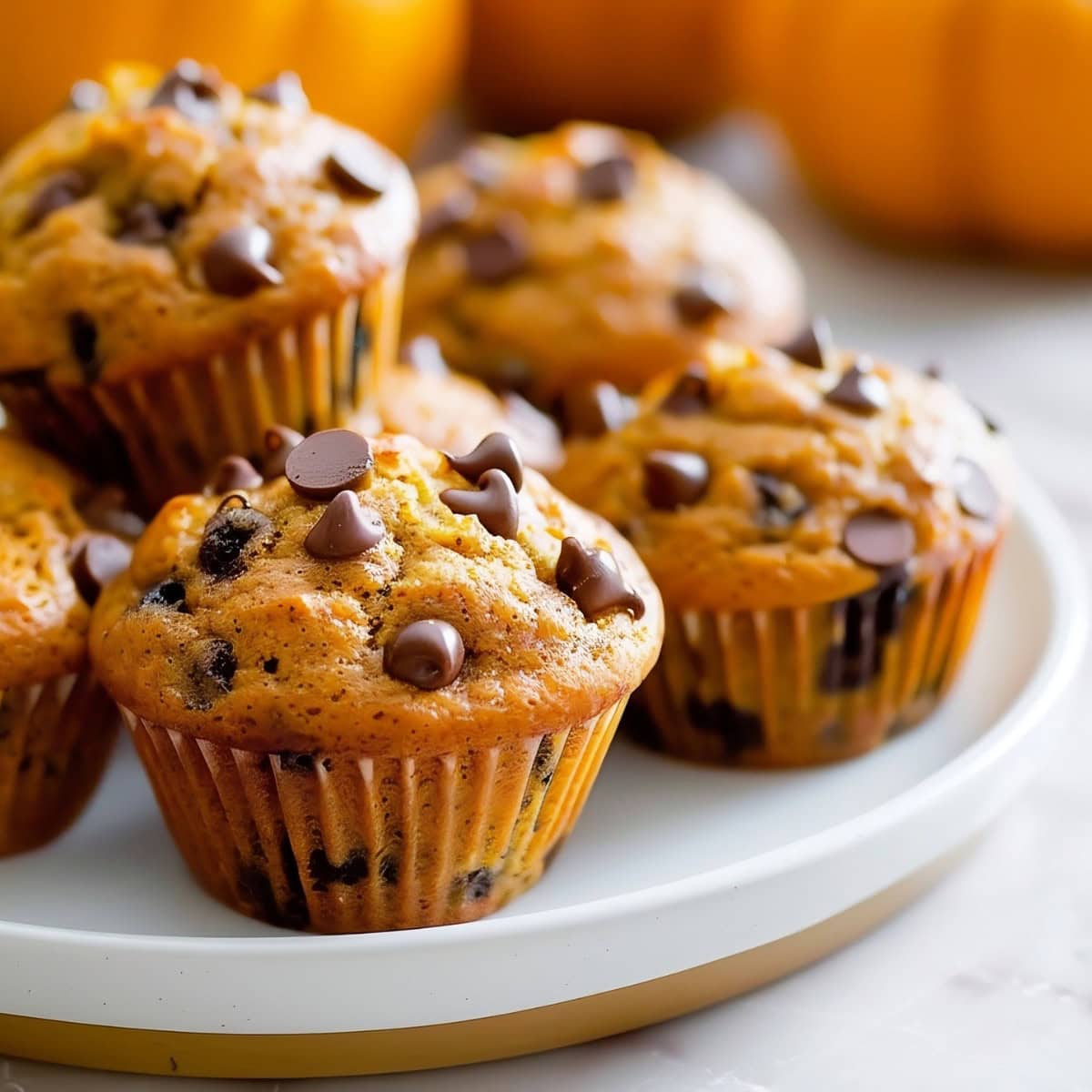 Close Up of Pumpkin Chocolate Chip Muffins, Stacked on a Plate with Pumpkins in the Background