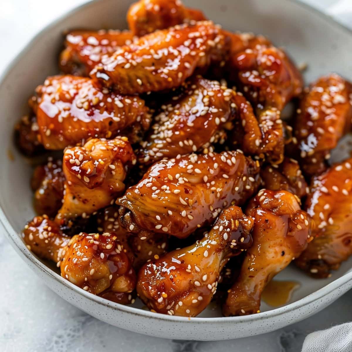 Savory homemade honey garlic chicken wings in a white bowl on a white marble table.