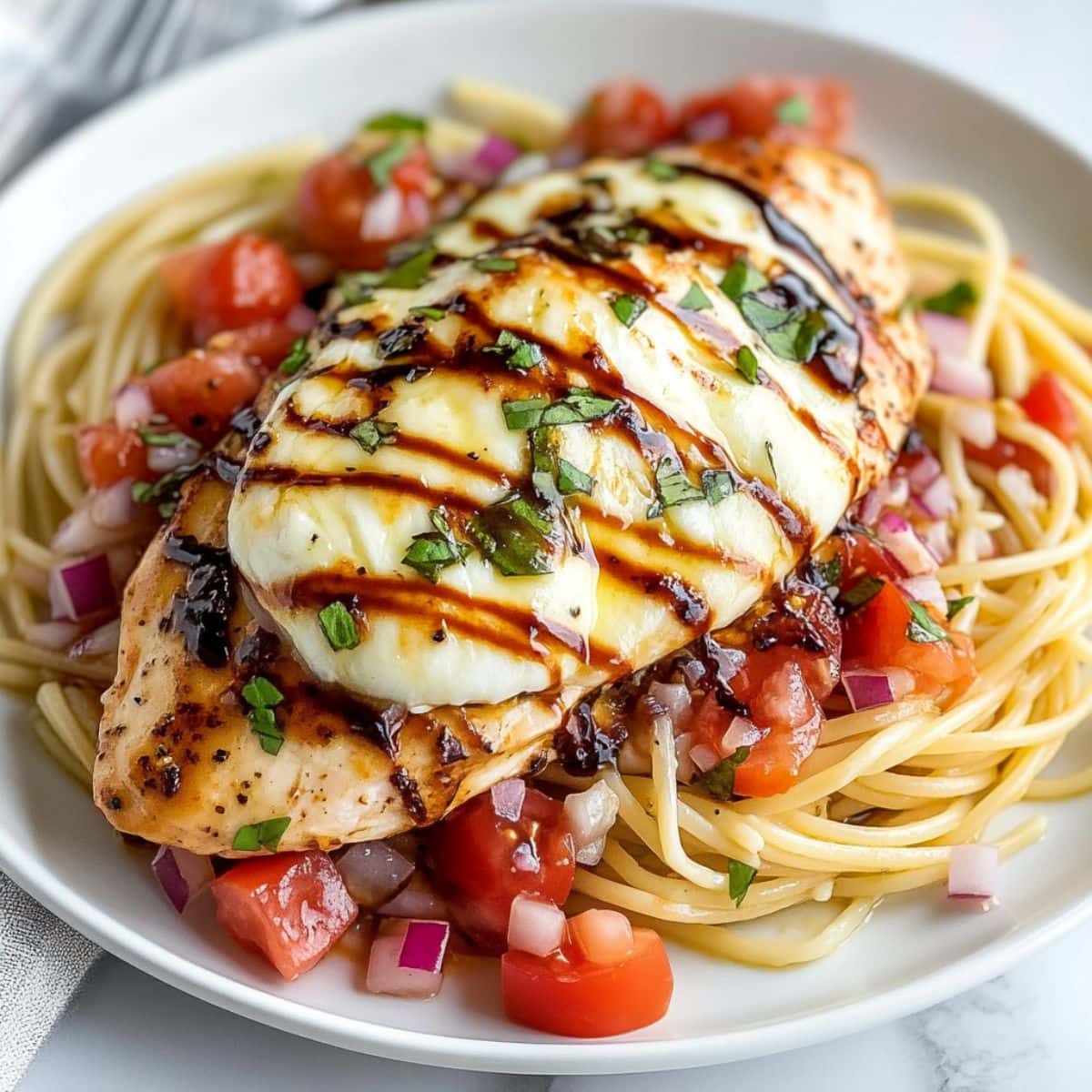 Pasta topped with bruschetta chicken drizzled with balsamic vinegar.