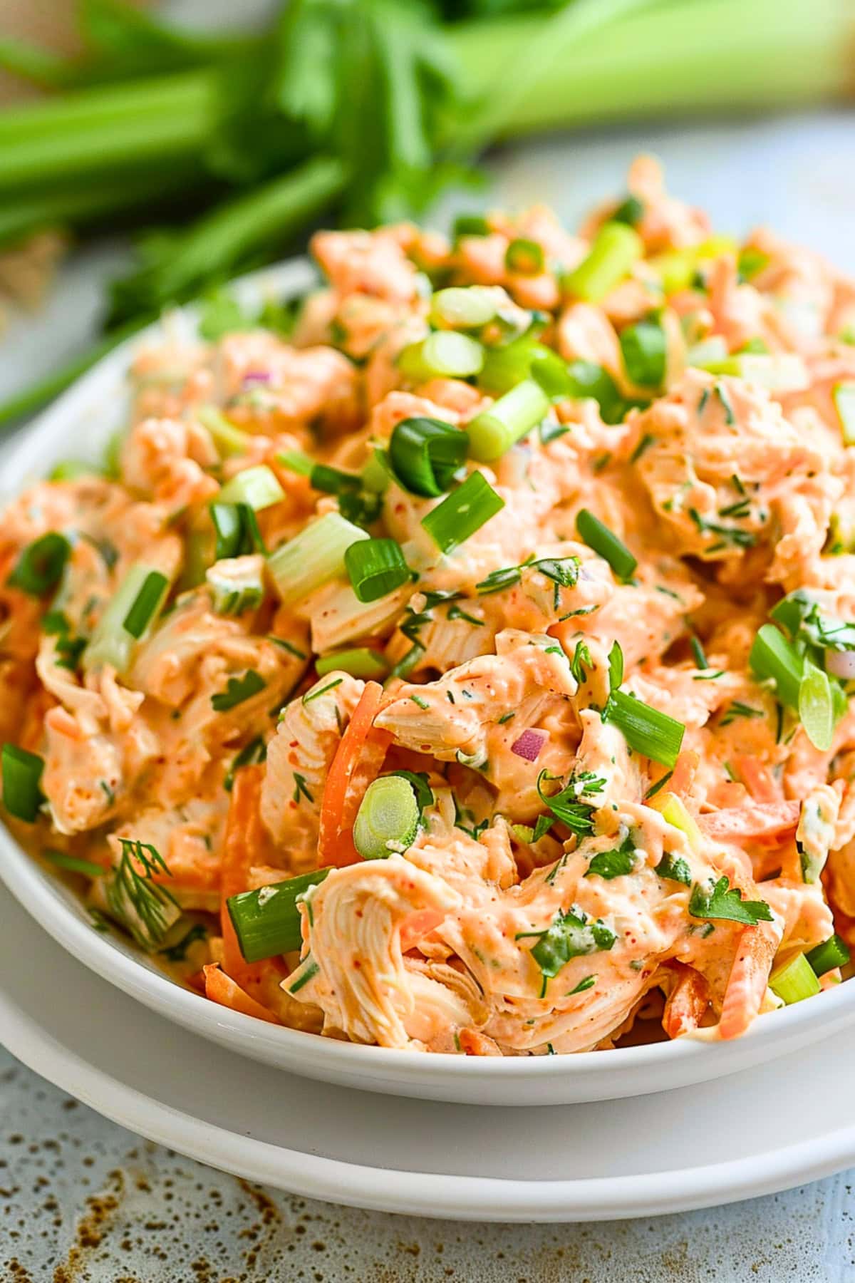 Buffalo chicken salad served on a white bowl garnished with chopped green onions.