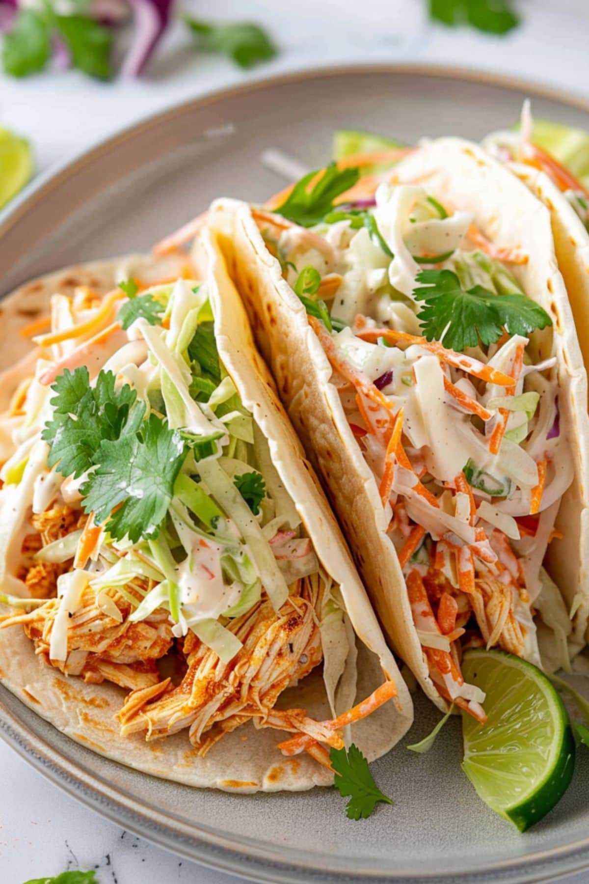 Tacos with shredded buffalo filling and shredded lettuce and carrots tossed in ranch dressing on top garnished with chopped cheddar cheese.