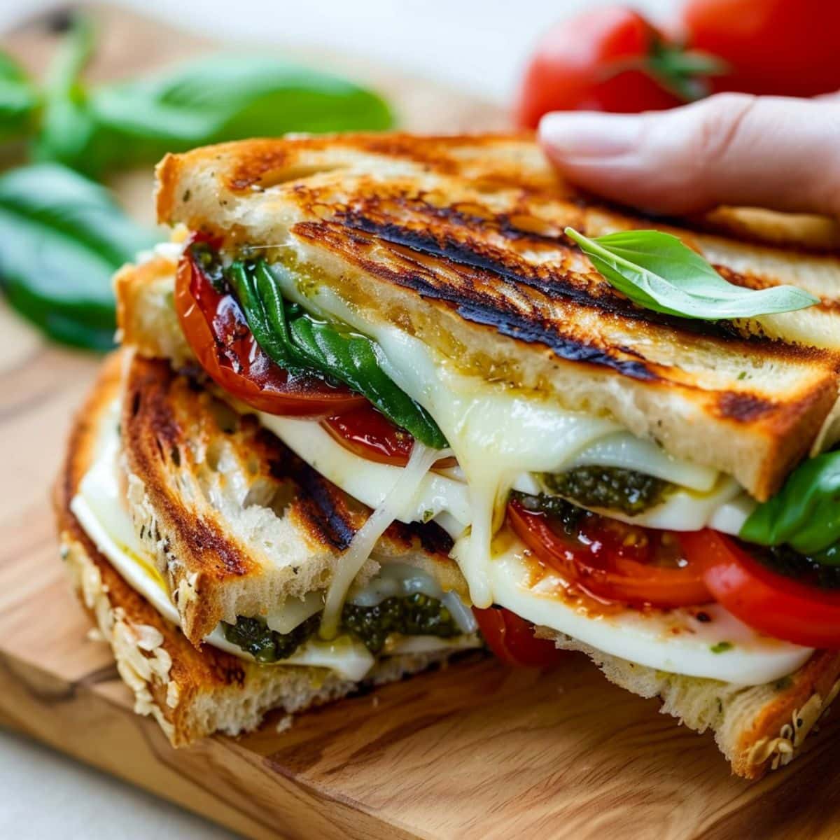 Hand holding cheesy caprese grilled cheese sandwich from a wooden board.