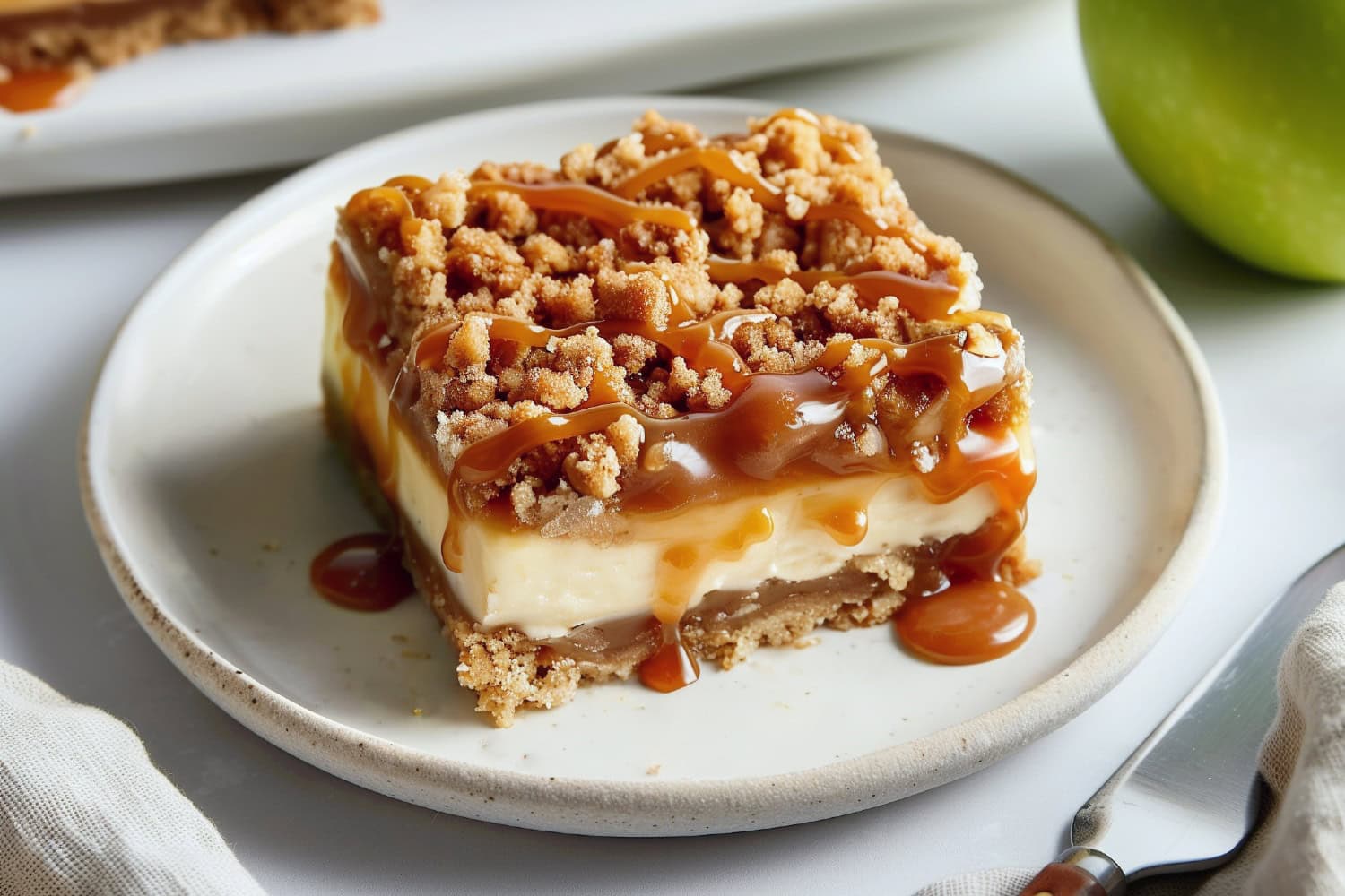 A plate of caramel apple cheesecake bar topped with streusel crumbs and drizzled with caramel sauce.