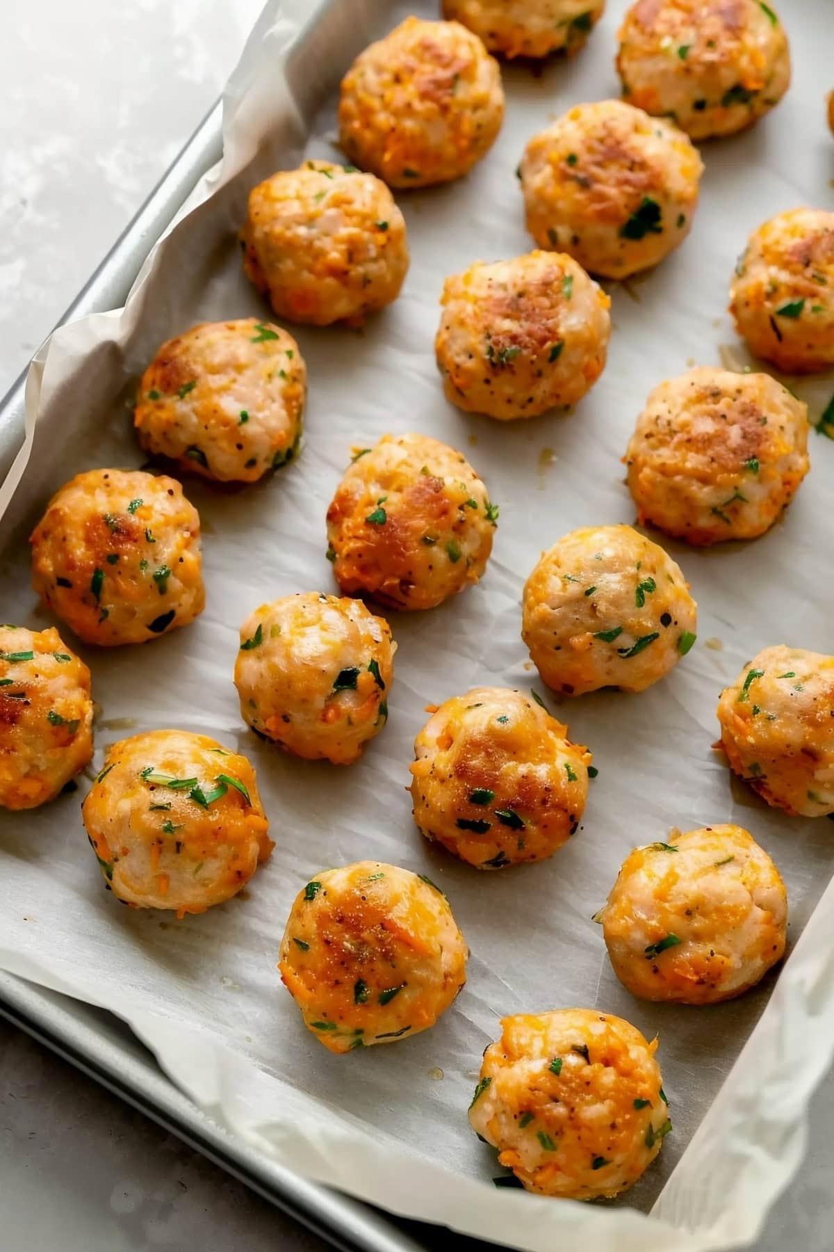 Homemade chicken meatballs on a baking tray with parchment paper.