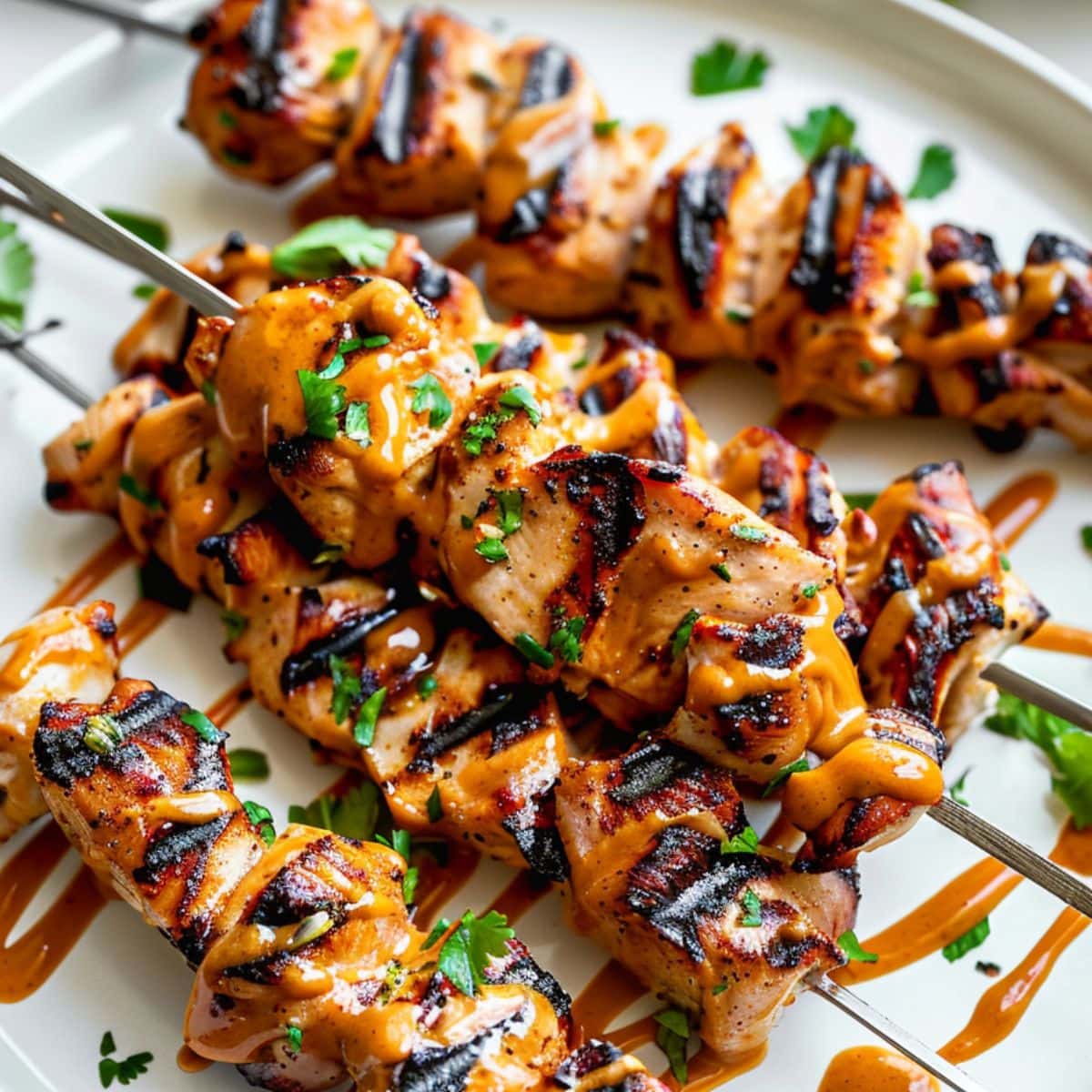 Chicken satay with drizzle of peanut butter sauce served on a white plate.