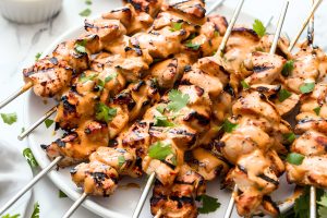 Chicken satay with peanut sauce served on a white plate.