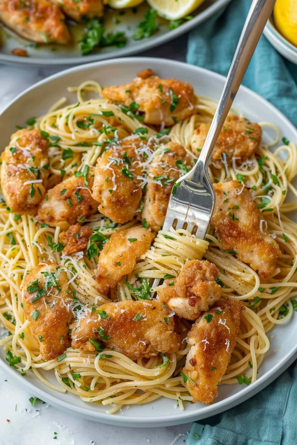 Fork twirling on a serving of chicken scampi served on a white plate on a white marble table. 