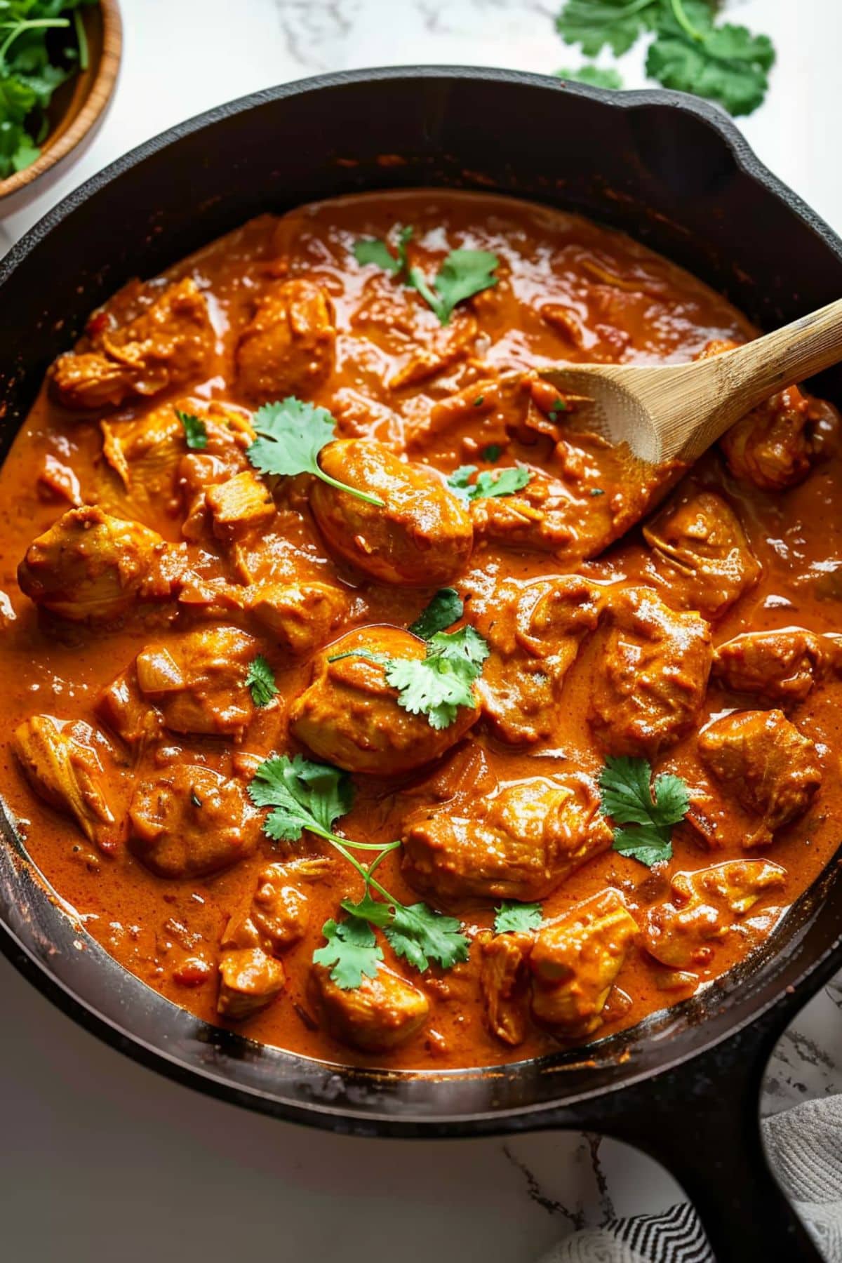 Wooden spoon in a cast iron skillet pan filled with chicken tikka masala.