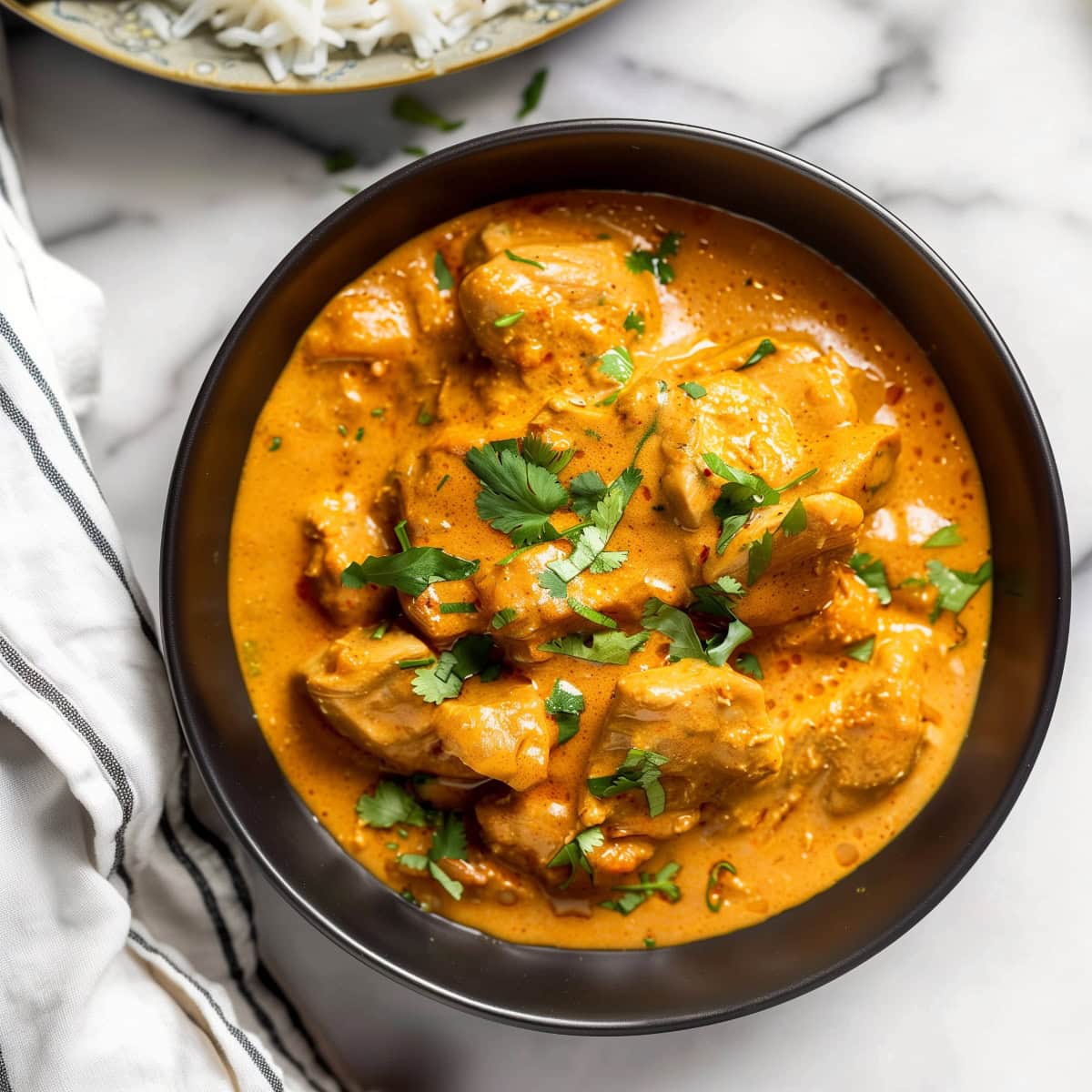 Flavorful coconut chicken curry in a bowl with a rich, aromatic sauce and fresh herbs, top down view